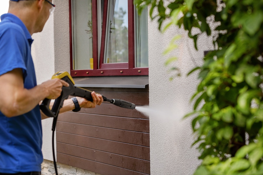 Professional exterior home cleaning expert uses pressure washer to remove dirt, grime, and mold from exterior of a home. 