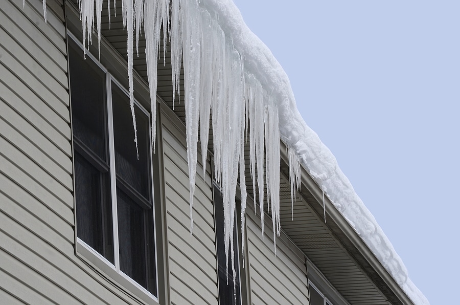 Close-up of a house with a snow-covered roof and long icicles hanging from the eaves and gutters.